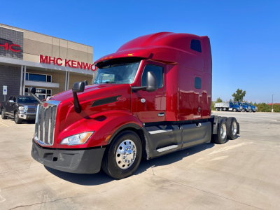 Peterbilt 579 sleeper cab tractor in red, side view showing front grille, bumper, chrome wheels, and dual rear axles in a dealership lot.