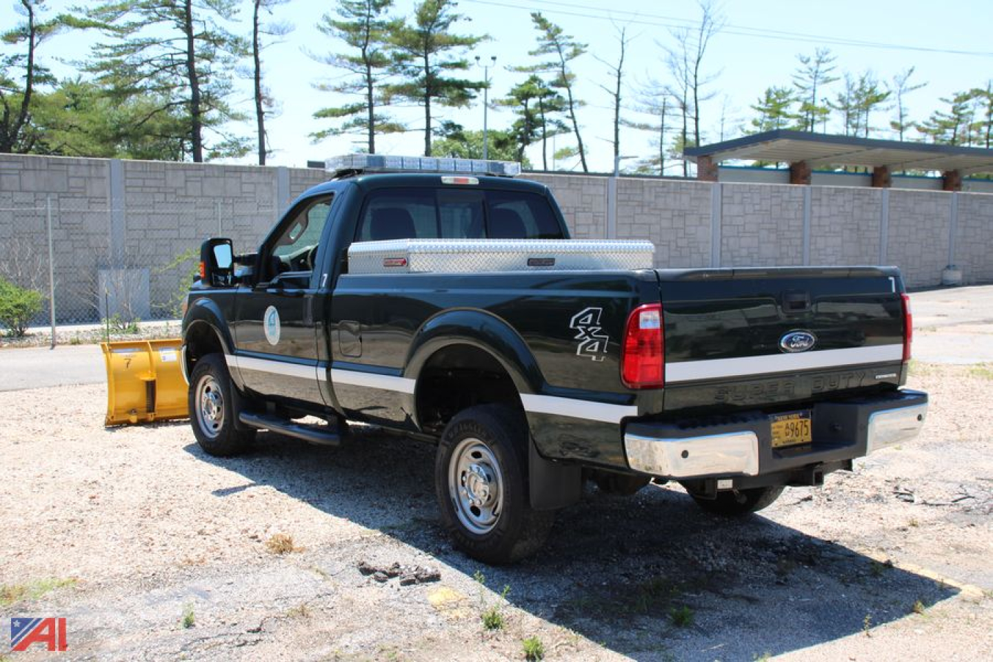 Ford F-250 Super Duty pickup with plow seen from rear three-quarter view; long bed, toolbox, dually? Actually single rear axle; black truck with chrome bumper and side steps, plow off to left.