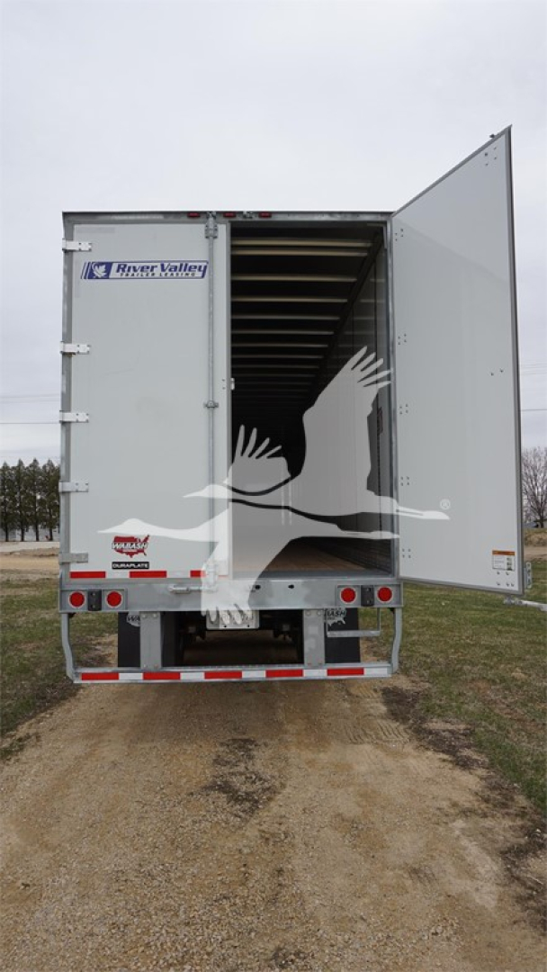 Trailer rear open showing Wabash Duraplate sticker and tail lights. Branding stickers on left side of doors, speckled dirt and open cargo area.