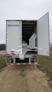 Trailer rear open showing Wabash Duraplate sticker and tail lights. Branding stickers on left side of doors, speckled dirt and open cargo area.
