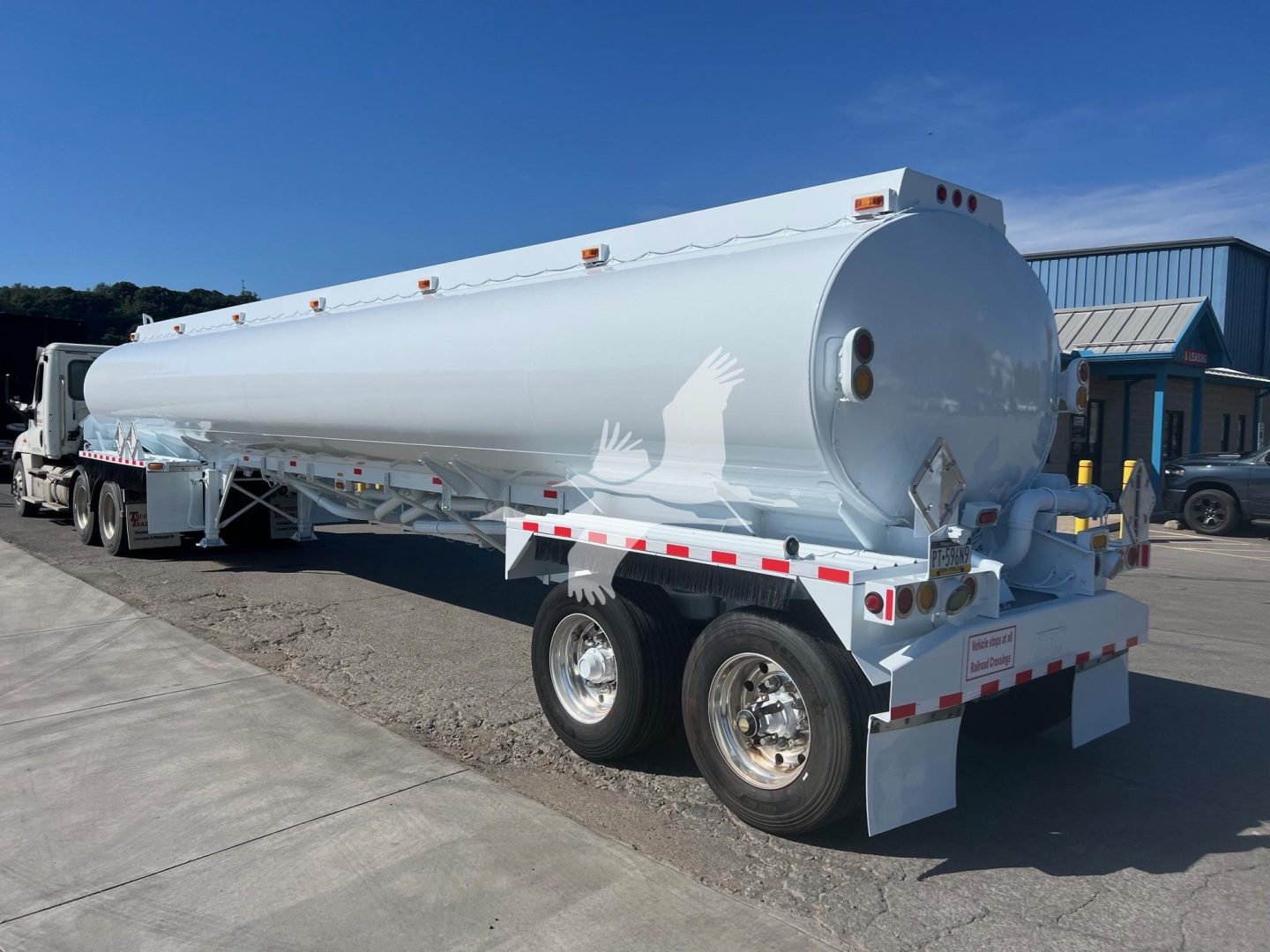 Tank trailer showing cylindrical tank and rear equipment with dual rear axles, white paint, ladders and safety reflectors.