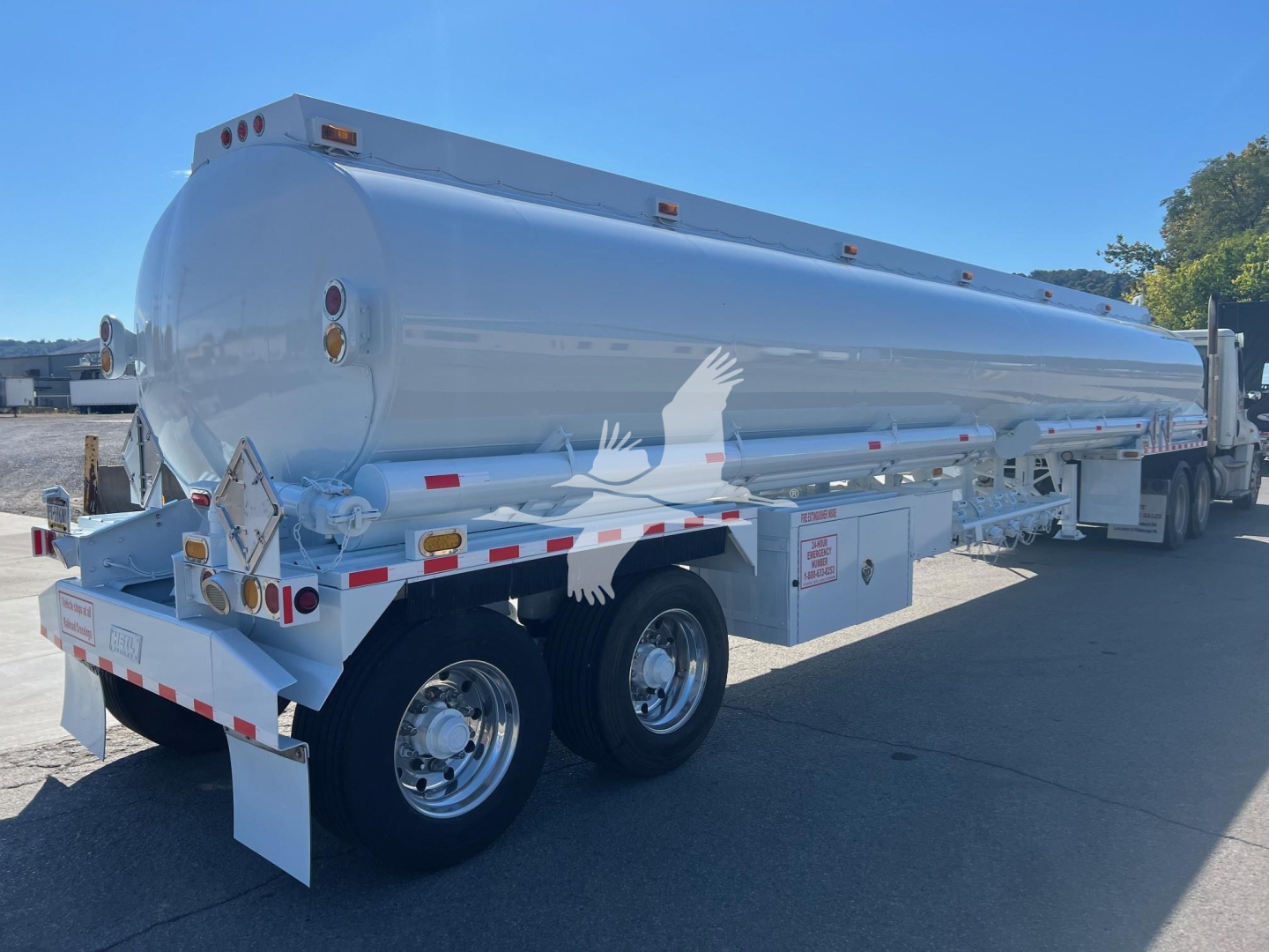 Fuel tanker trailer showing cylindrical tank mounted on dual rear axles with reflective tape and safety decals.