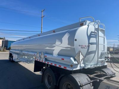 Tank trailer showing a white Heil Petro Tank with dual rear wheels and safety ladders; side graphic of flying birds and a circular rear end with supports and reflective strips.