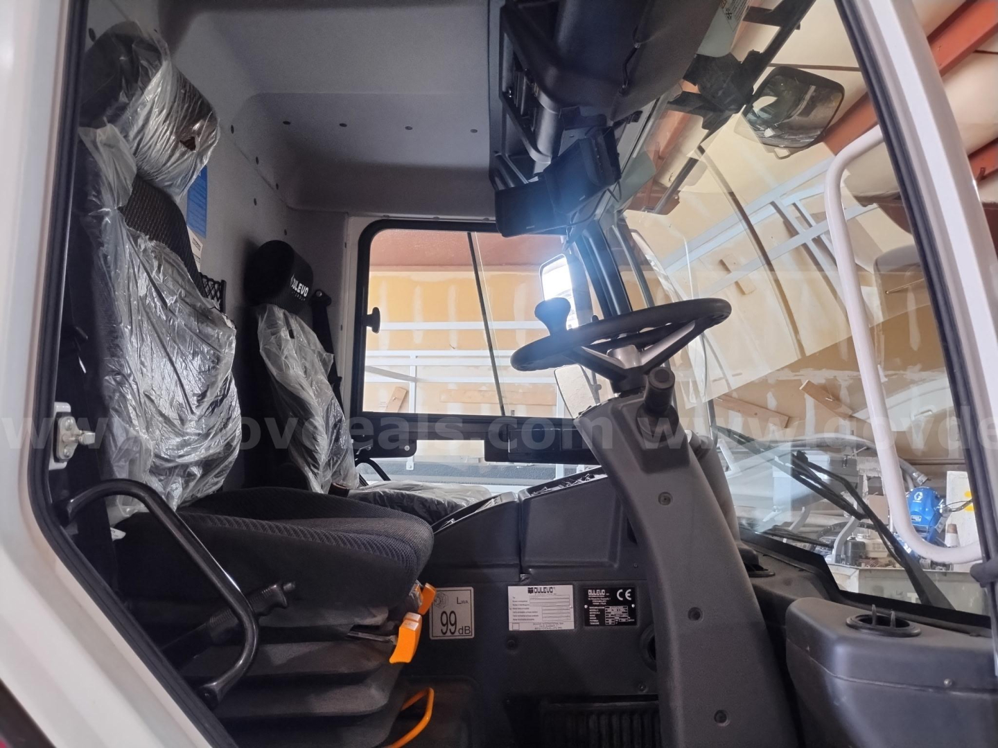Elgin 6000 sweeper truck cab interior showing steering wheel, driver seat, dashboard controls, and windshield with side door.