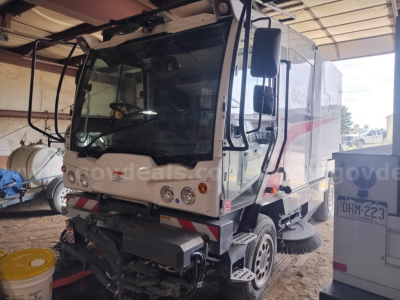 Elgin 6000 sweeper truck front-left view with cab and side brush, stock number 31488-1 visible, outdoor storage area.