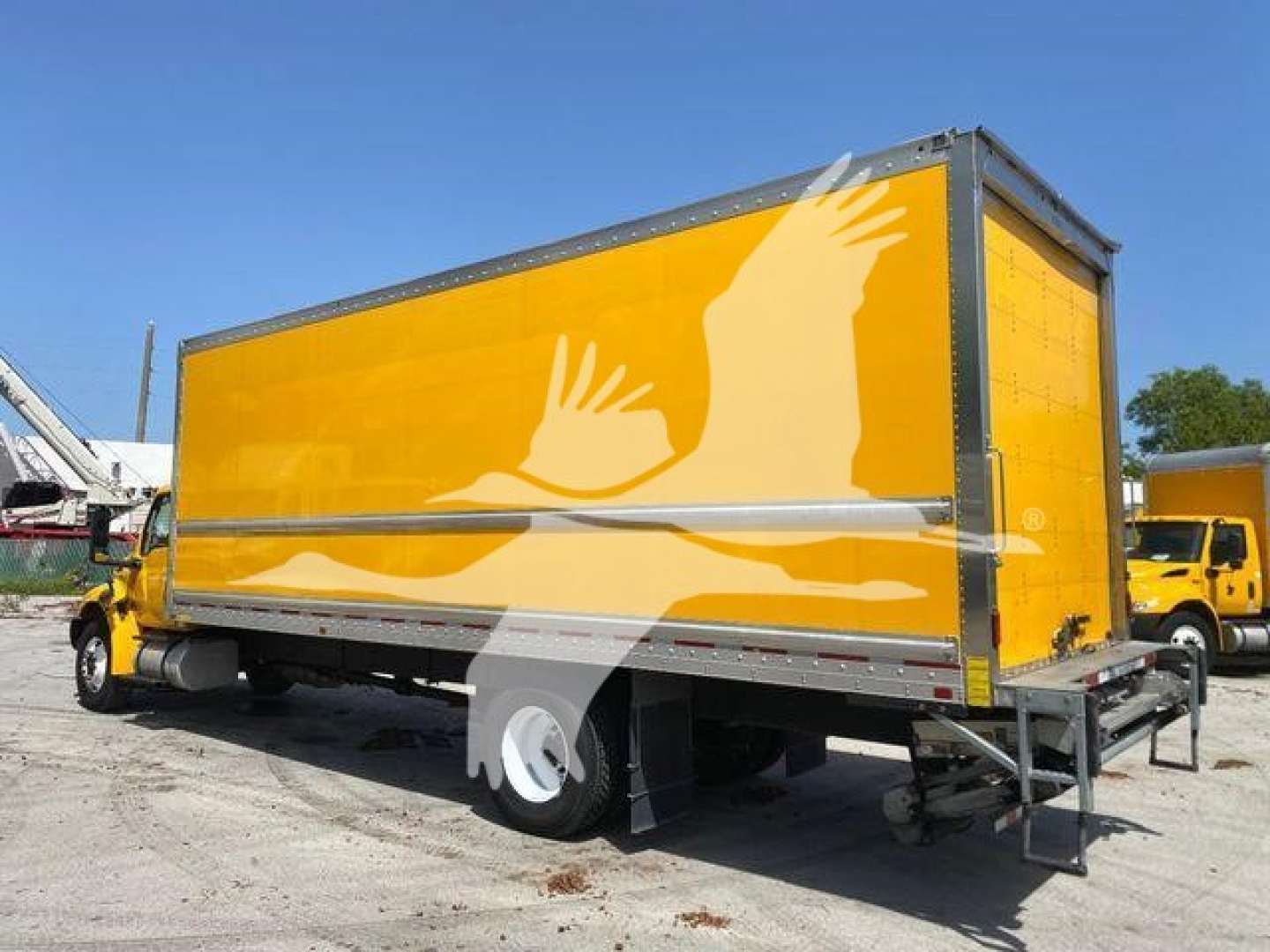 Box truck with yellow cargo body and graphic of white hands on side, International MV appears in a yard.