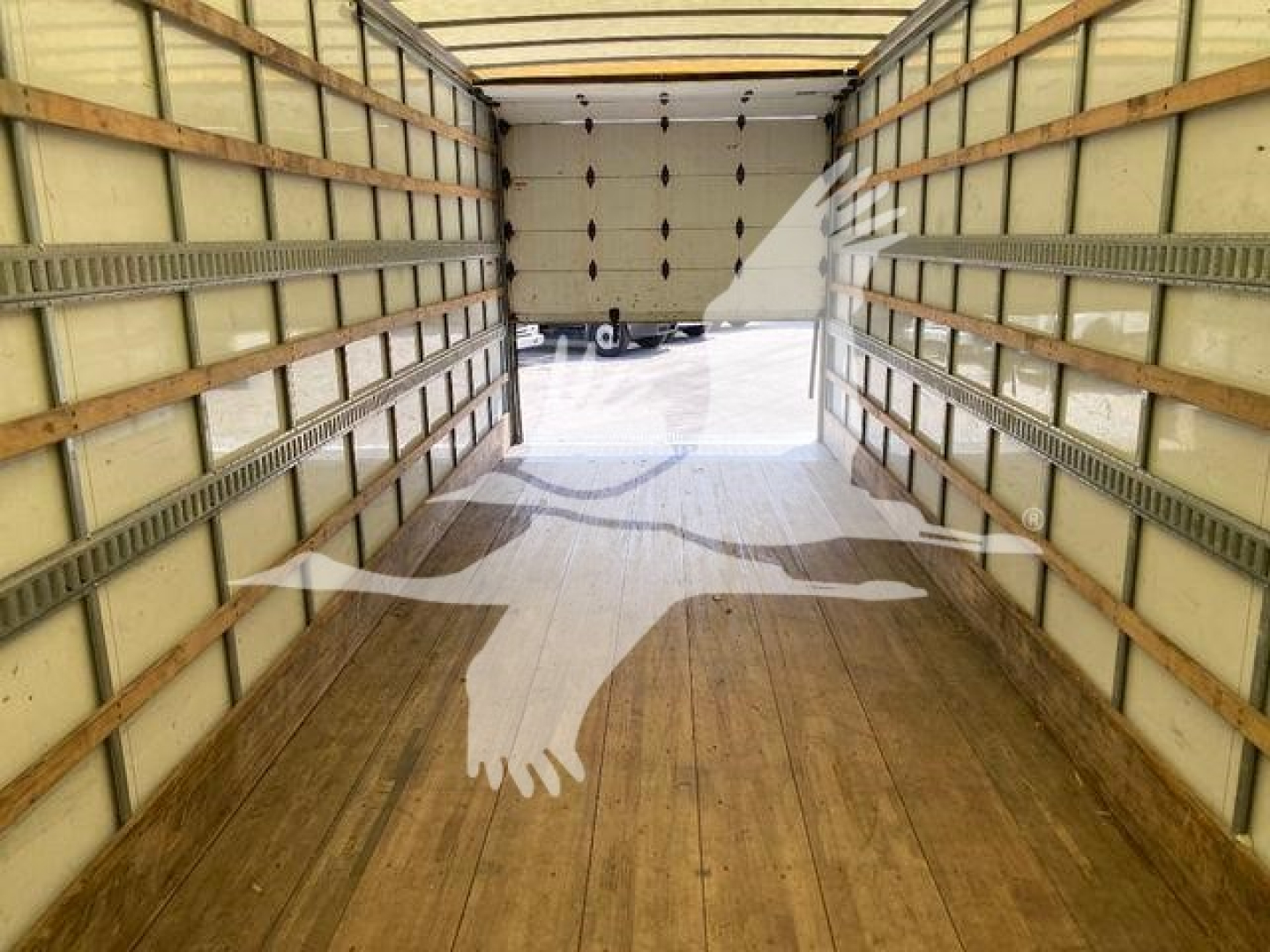 Interior trailer view: empty box truck cargo area with wooden floor and side metal rails, open back door showing driveway and another vehicle.