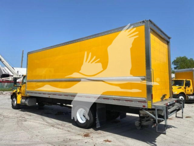 Box truck with yellow cargo body and graphic of white hands on side, International MV appears in a yard.