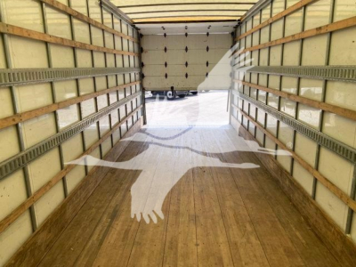 Interior trailer view: empty box truck cargo area with wooden floor and side metal rails, open back door showing driveway and another vehicle.