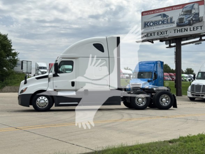 Freightliner Cascadia 126 sleeper cab, side view, with white exterior and chrome wheels, parked in lot. Visible freight company sign in background.