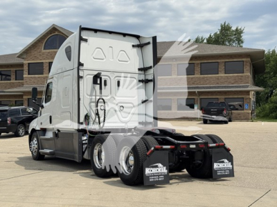 Freightliner Cascadia 126 sleeper truck rear view showing chassis and rear wheels, white cab, dealership lot in background.