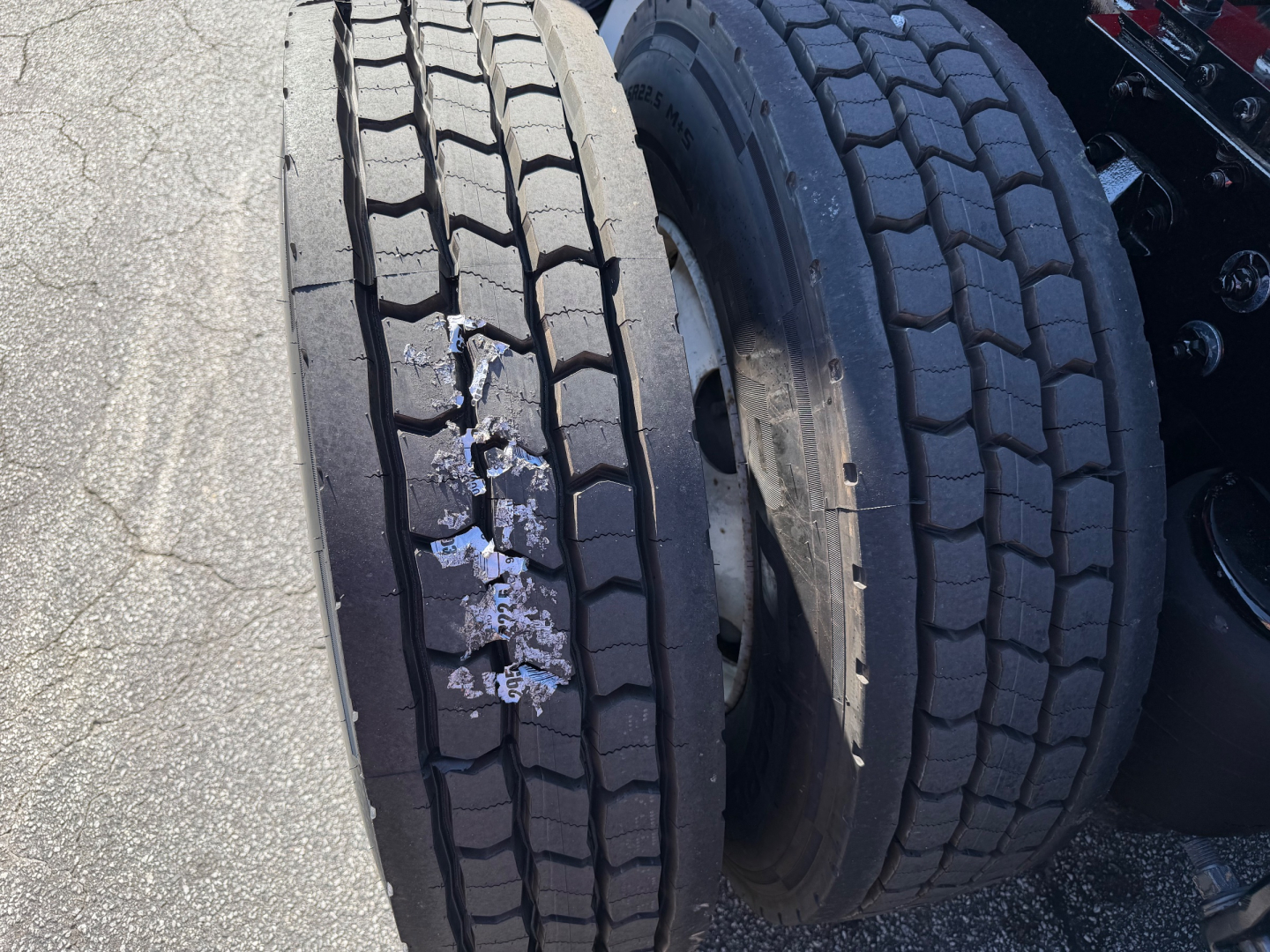 Truck axle showing dual rear tires with tread wear and a damaged inner tire. Visible are two sets of heavy-duty tires mounted on a Kenworth T680 tractor.