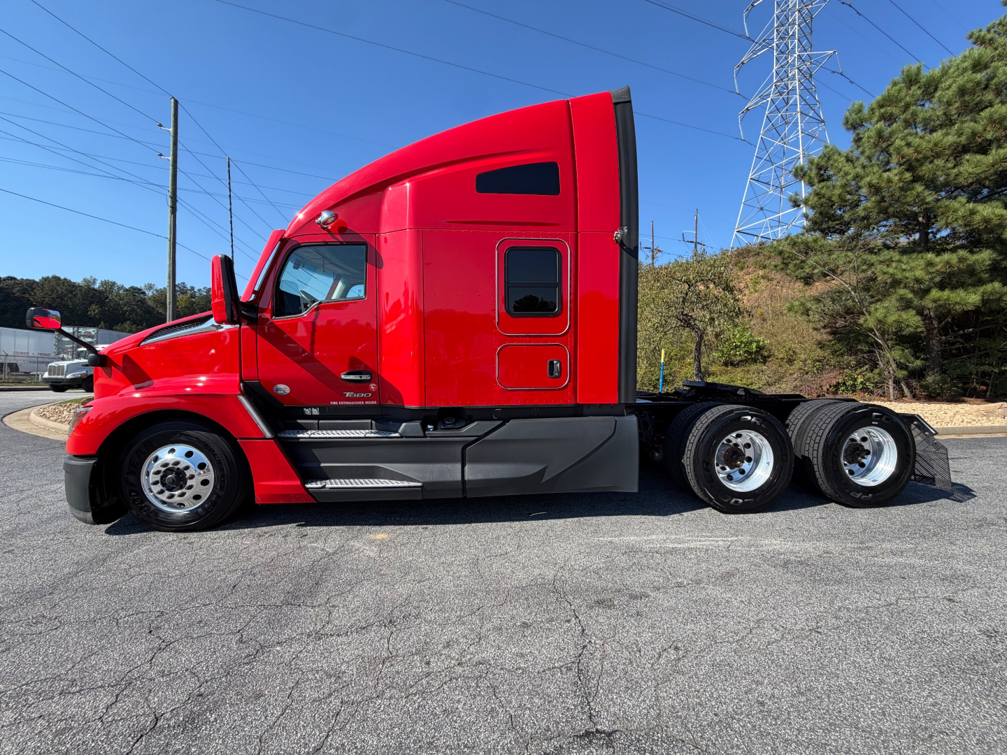 Kenworth T680 side profile showing red cab, sleeper, black chassis, and three rear axles. Visible text on cab includes Kennworth badge and model details.