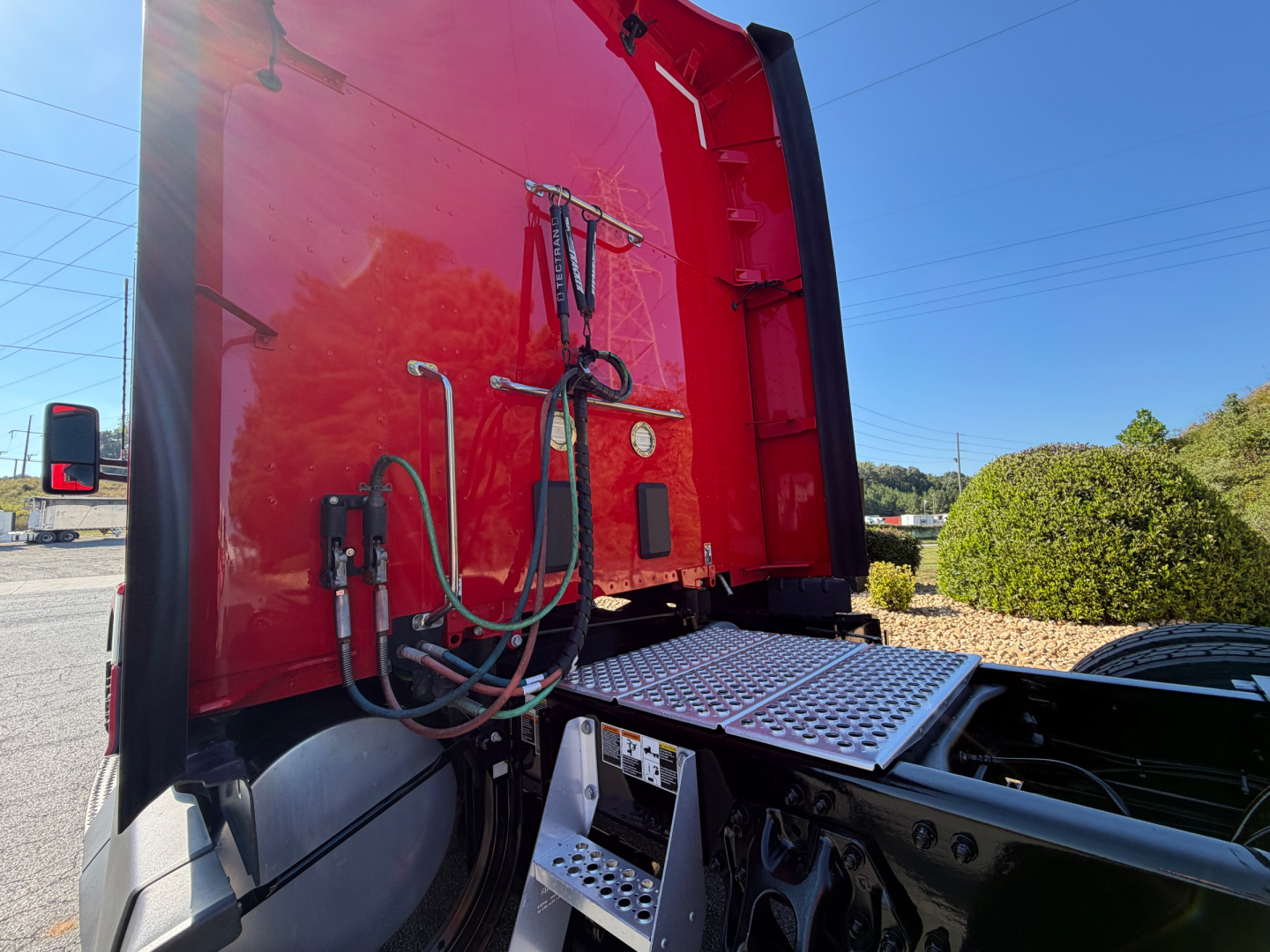 Kenworth T680 truck rear view showing access panel and hydraulic lines near sleeper, red cab with metal diamond-plate step.
