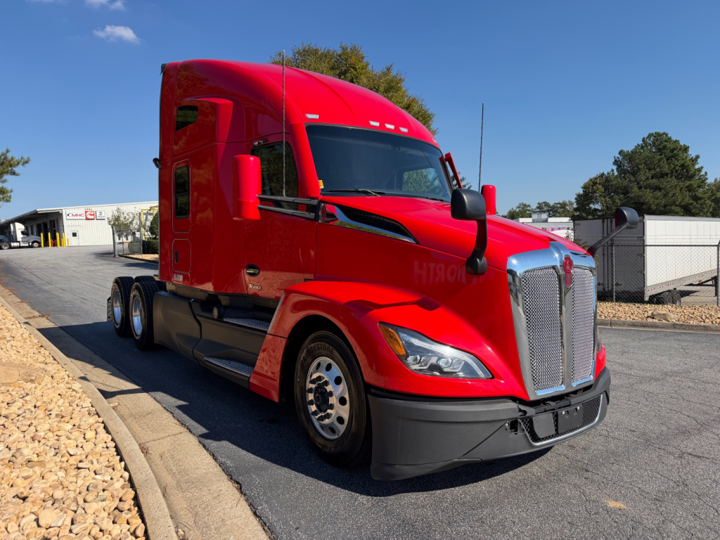 Red 2023 Kenworth T680 tractor-trailer cab in-service showing front grille, headlights, and side window; no visible text on the cab.