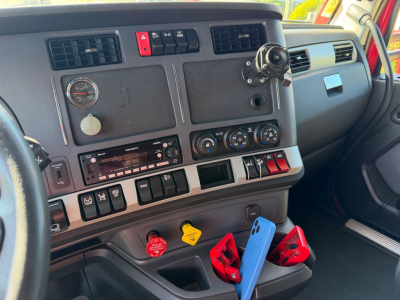 Kenworth T680 truck interior dashboard view showing gauges, controls, and gear selector with red and yellow handles visible.