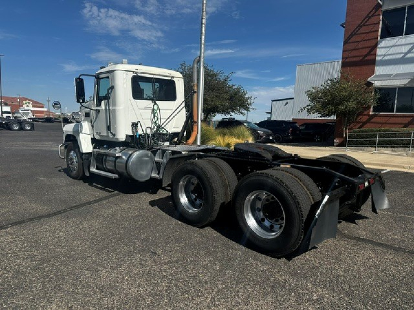 Truck chassis and cab of a 2020 Mack PI64T with white cab and dual rear axles, visible fuel tanks, and side exhaust, parked in a lot.