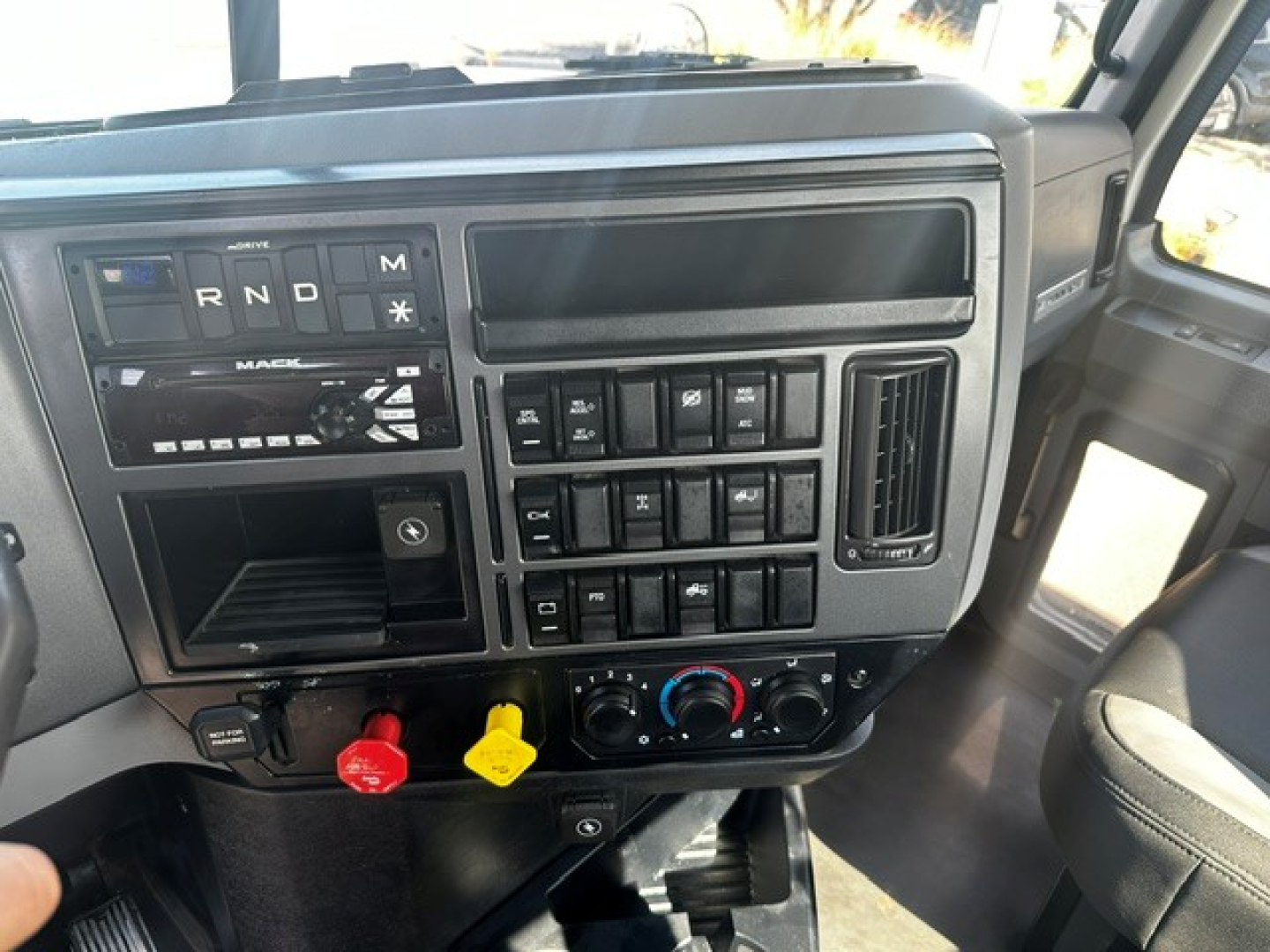 Dashboard of a 2020 Mack PI64T showing R N D M shift indicators, various switches, red and yellow knobs, and climate controls.