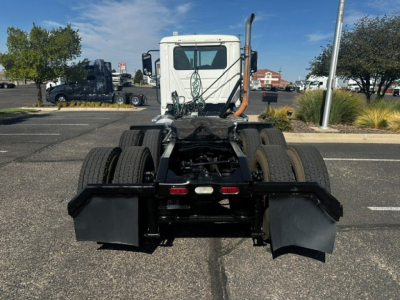 Truck chassis with rear view showing dual rear axles and mud flaps on a white cab; spare lines and connectors visible; rear frame and fifth wheel mount area, parking lot background.