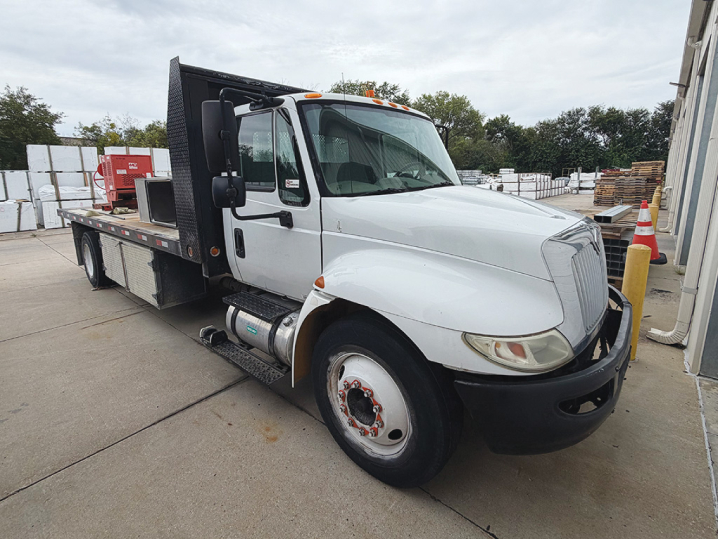 2009 International 4300 conventional daycab truck with a flatbed/duty bed and black equipment racks in a yard.