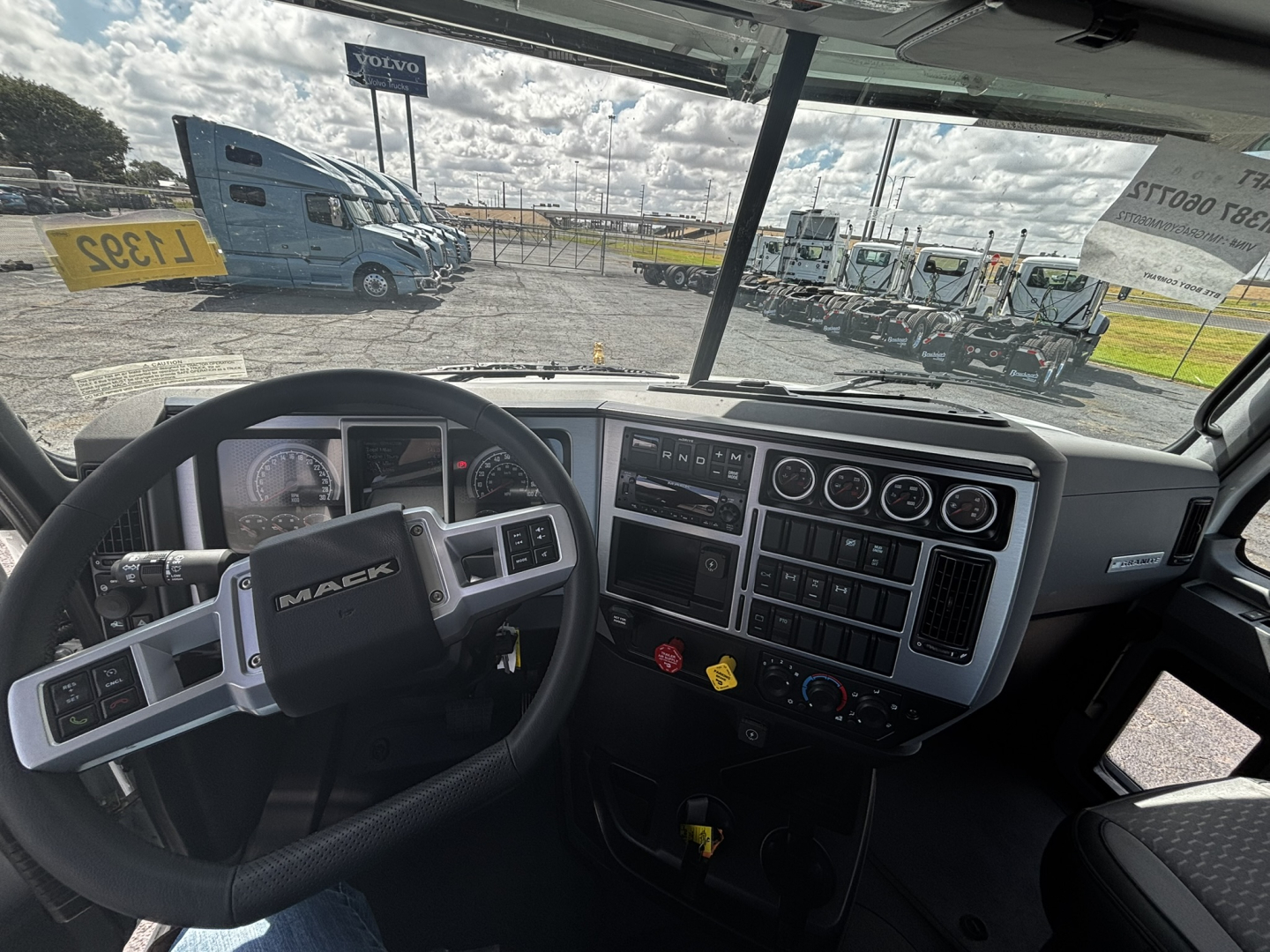 Cab interior of a 2027 Mack GR64FT shows steering wheel, gauge cluster, and dashboard with multiple control panels and vents.