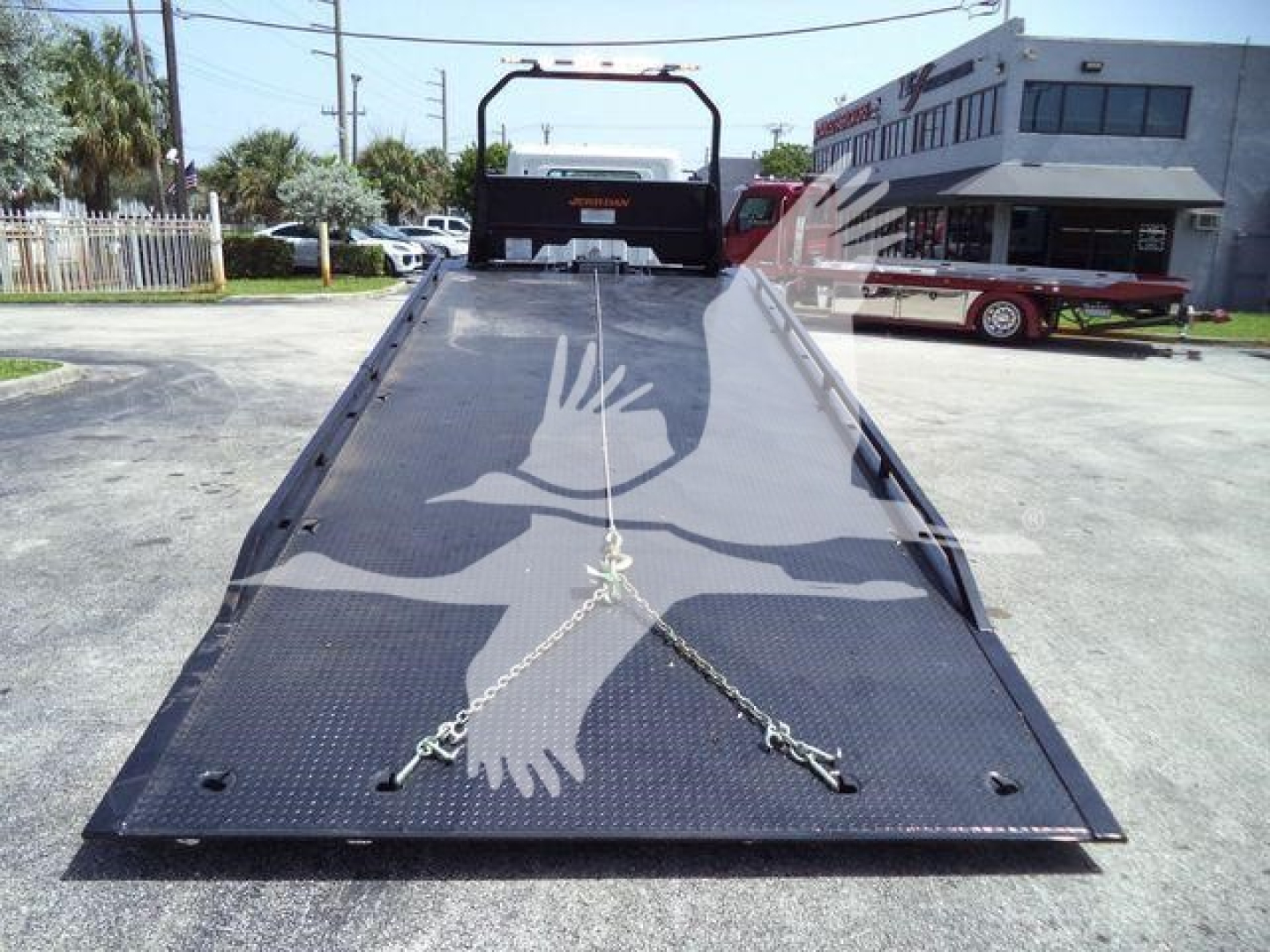 Flatbed truck ramp showing a chain tie-downs and non-slip surface with D-shaped cutouts and a foldable railing at the end.