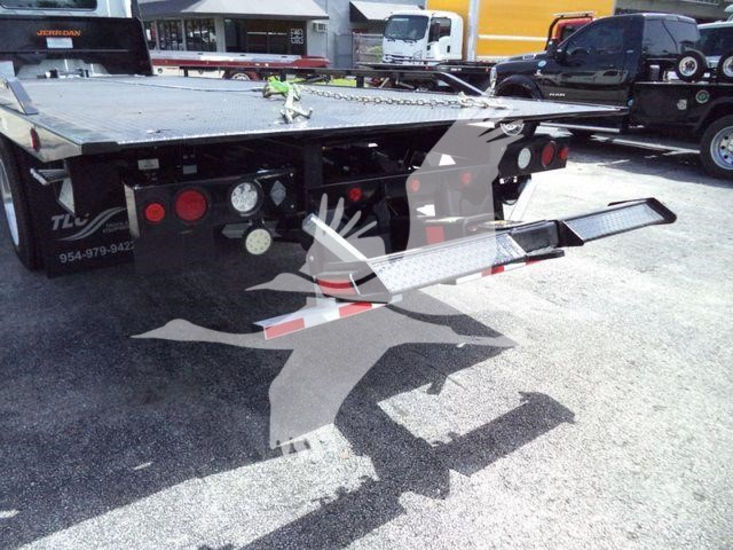 Flatbed tow truck trailer with rear deck and access steps; visible hydraulics, lights, and bumper. 2026 Hino L6 listing image with platform and tail section in lot.