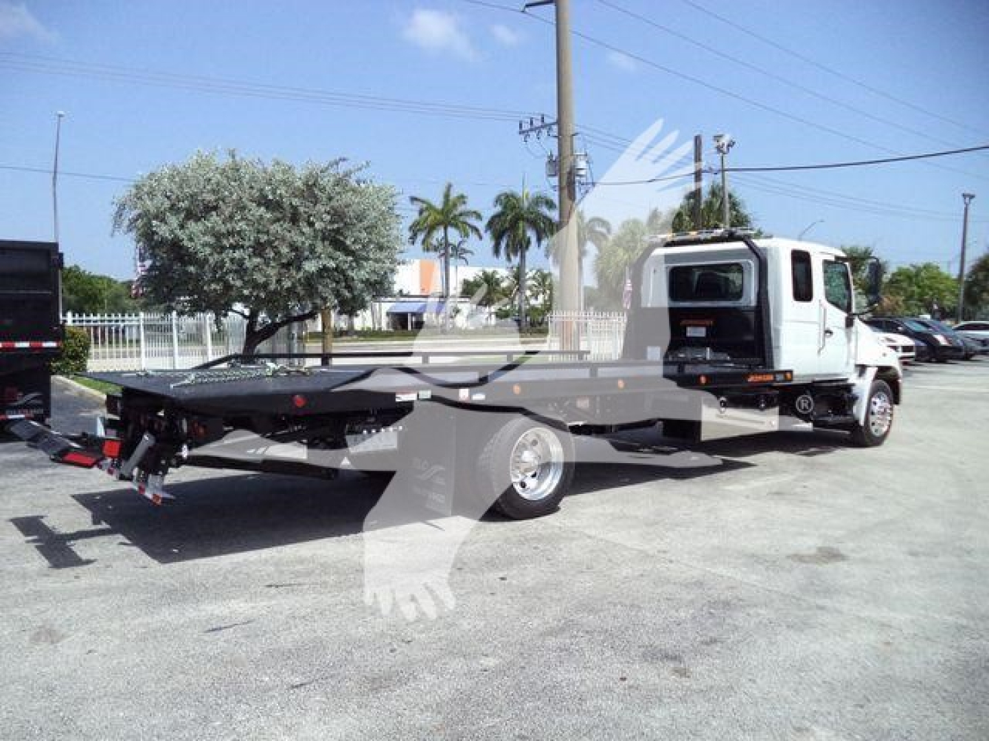 Truck tow/rollback vehicle with flatbed, cab in view, equipment and hydraulic lines visible on the flatbed; no visible text labels readable.