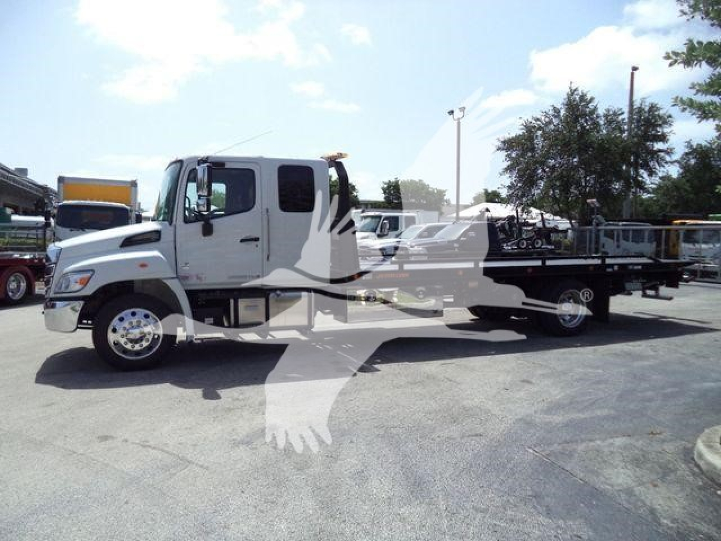 White Hino L6 rollback truck in a dealership lot, side view with flatbed; overlay watermark of a bird logo on the image.
