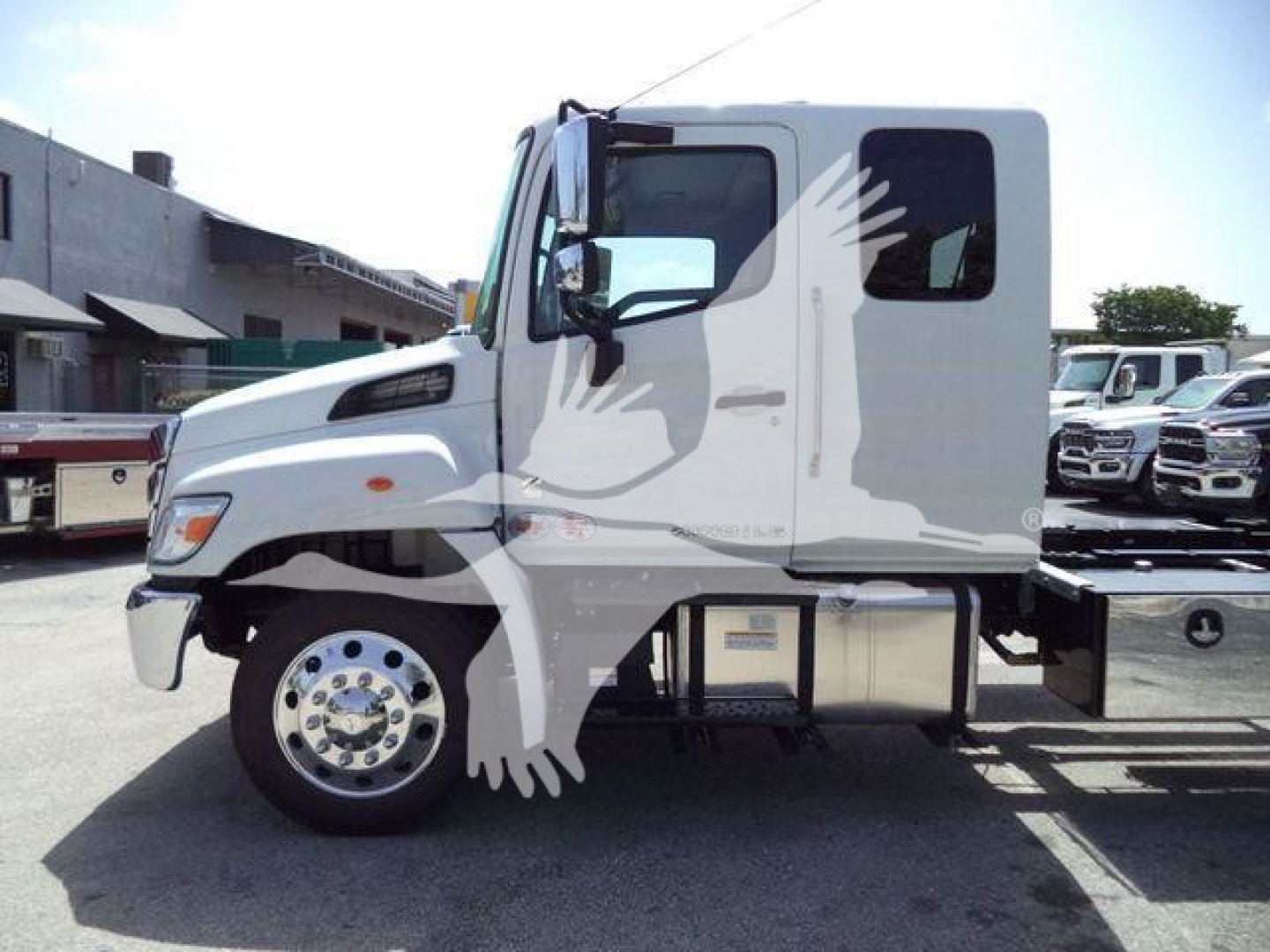Truck side view showing cab and chassis of a white Hino L6 with large front wheel, side mirror, and fuel/auxiliary compartments under cab.