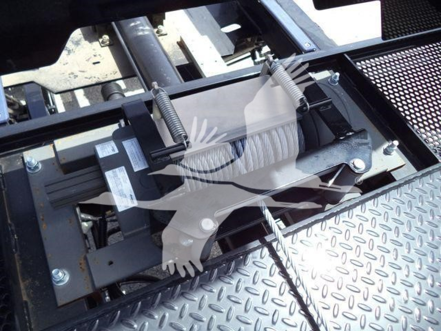 Truck bed entry showing hydraulic winch motor and roller fairlead assembly with spring-loaded mechanism and textured diamond plate surface.