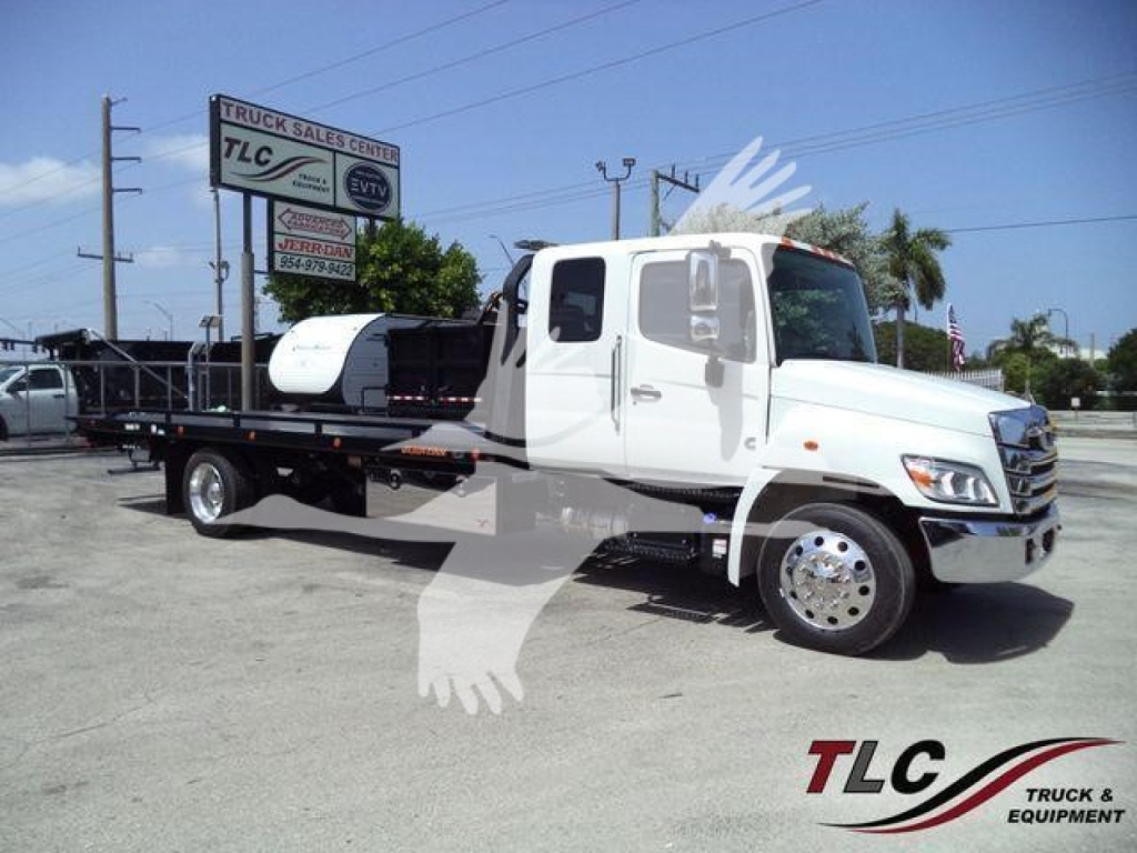 Front right side view of a white 2026 Hino L6 rollback tow truck with flatbed, cab doors, and large mirrors.