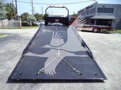 Flatbed truck ramp showing a chain tie-downs and non-slip surface with D-shaped cutouts and a foldable railing at the end.