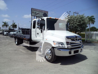 Truck bed tow truck with white cab and flatbed, front grille chrome, Hino emblem, daytime.