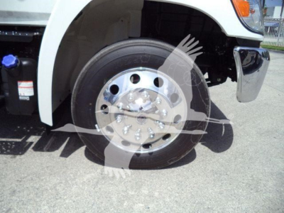 Truck front wheel and fender showing aluminum front wheel and tire on a white cab; visible hydraulic reservoir cap and chrome bumper area.