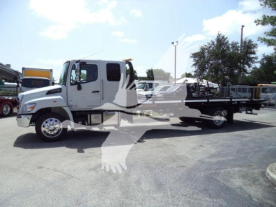 White Hino L6 rollback truck in a dealership lot, side view with flatbed; overlay watermark of a bird logo on the image.