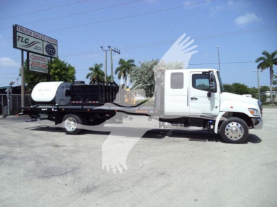Truck with flatbed rollback tow configuration showing cab and wheel set, dealership signs in background.