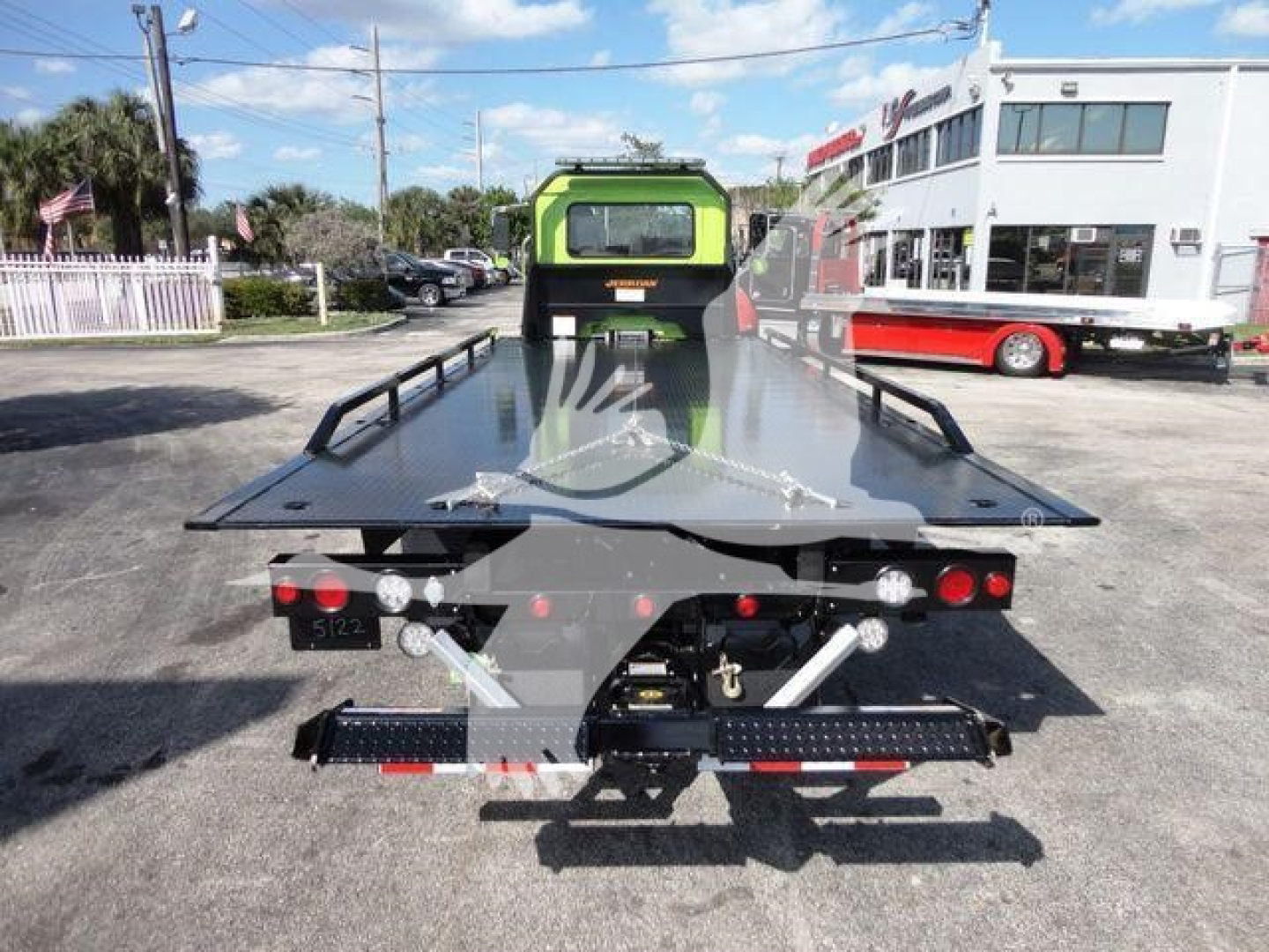 Flatbed tow truck bed showing rear view with hydraulic tilt mechanisms, taillights, and safety chains. The back of the truck includes a winch and mounting hardware.
