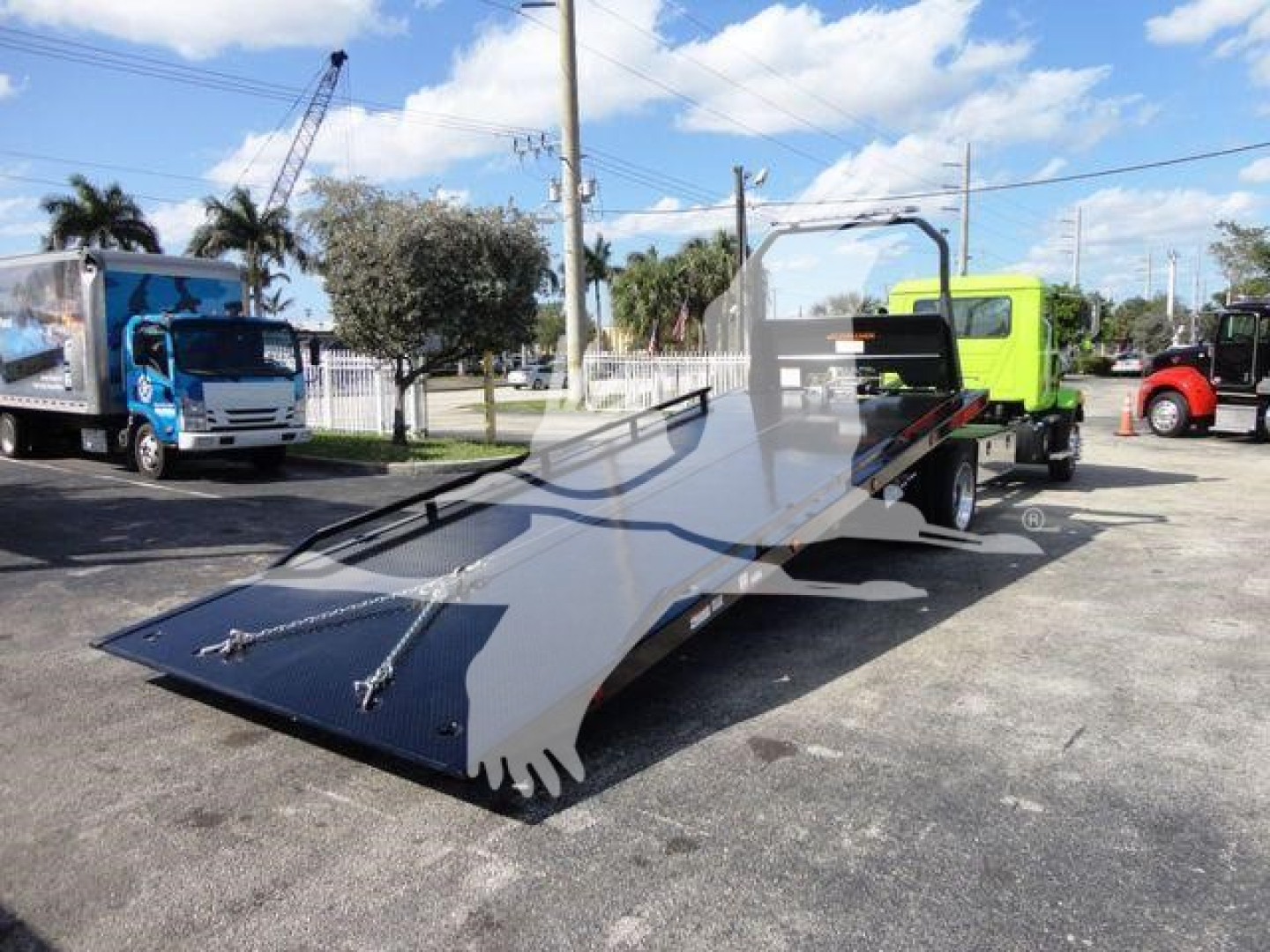 MD6 rollback truck with flatbed ramp ready for loading, side view showing green truck cab and other vehicles in lot.