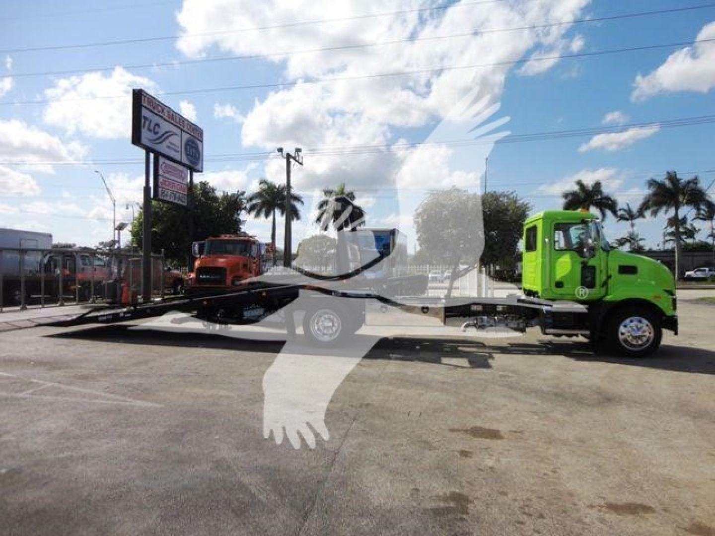 2026 Mack MD6 rollback truck on a trailer being displayed in a dealership lot with palm trees and blue sky in background.