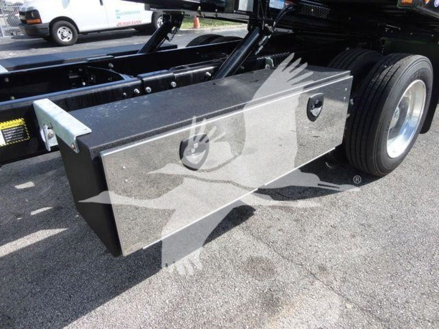 Truck chassis with large rectangular aluminum toolbox mounted near rear wheels, visible tire, undercarriage, and hydraulic lines. No legible serials or model numbers visible.