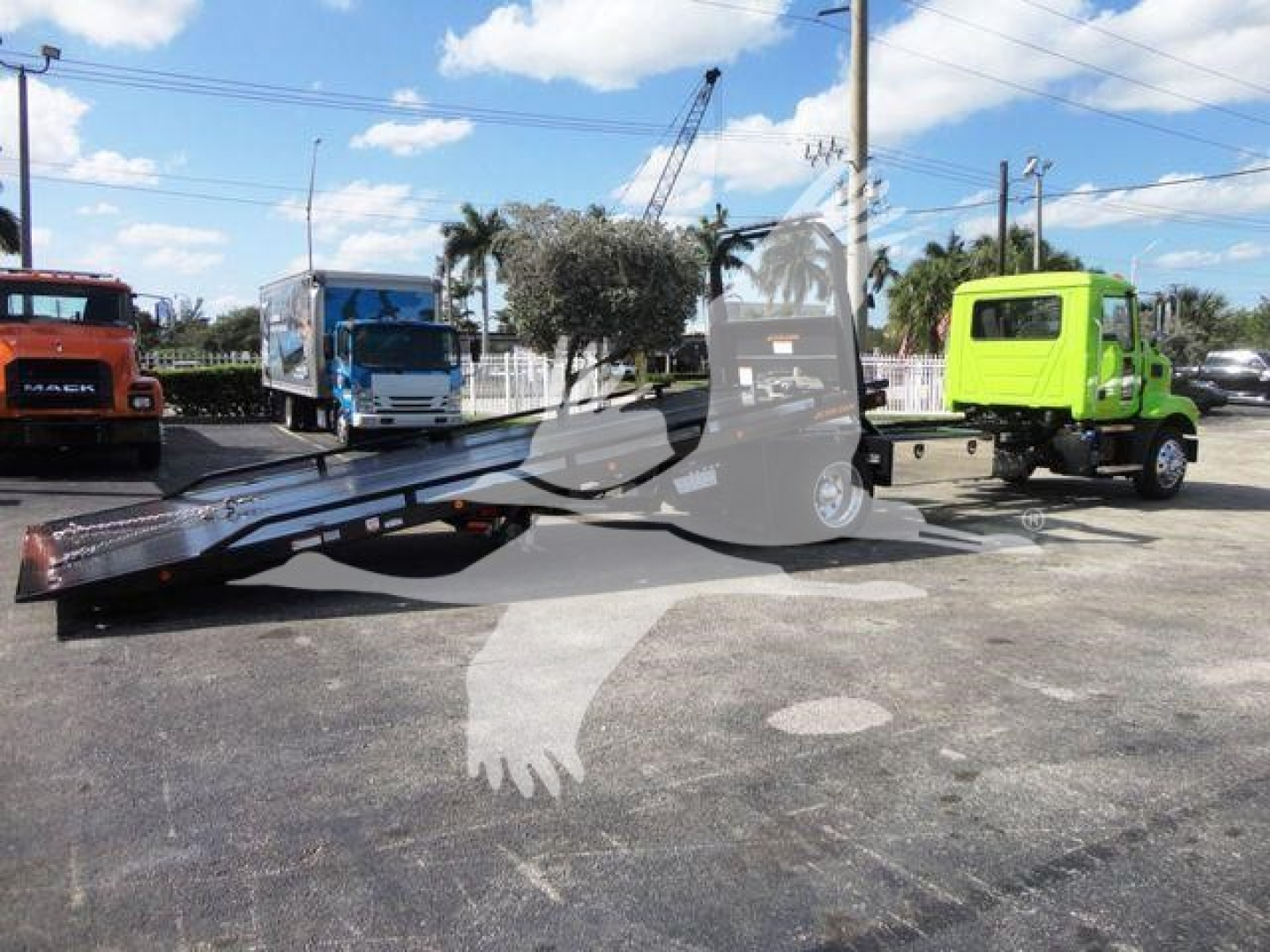 MD6 Mack tow truck in a dealership yard with a flatbed rollback, green and blue cab trucks in background.