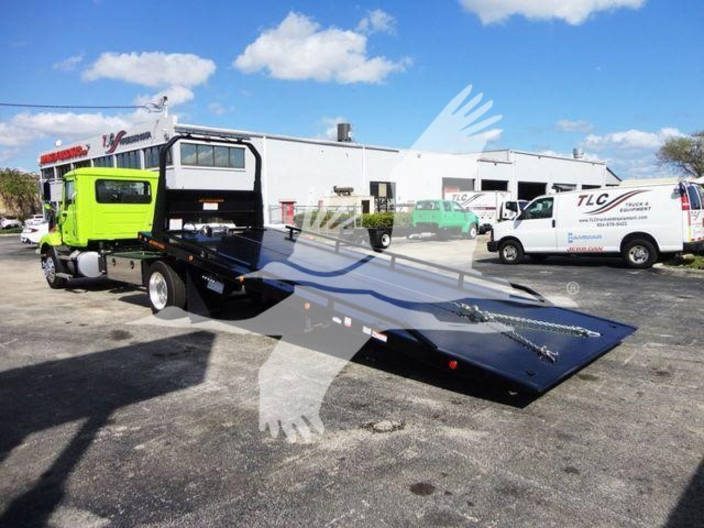 Flatbed tow truck with bright green cab and black ramp on a dealership lot.