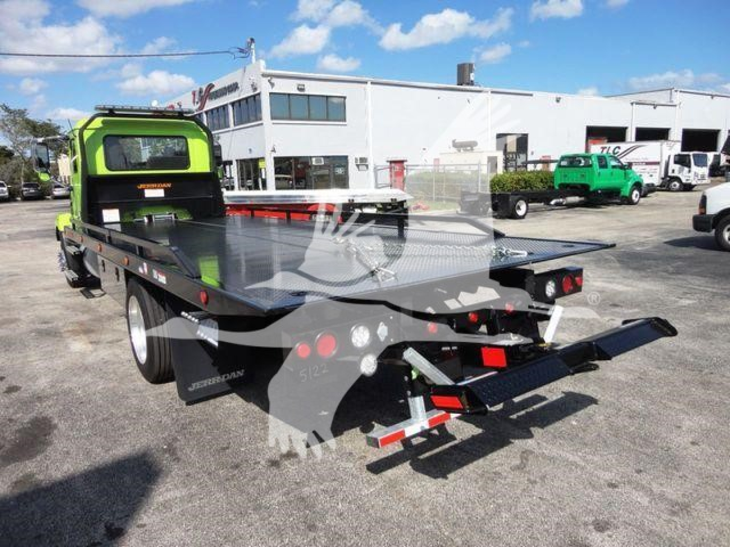 Mack MD6 rollback truck flatbed with green cab and dual rear ramps showing loader and flatbed equipment.