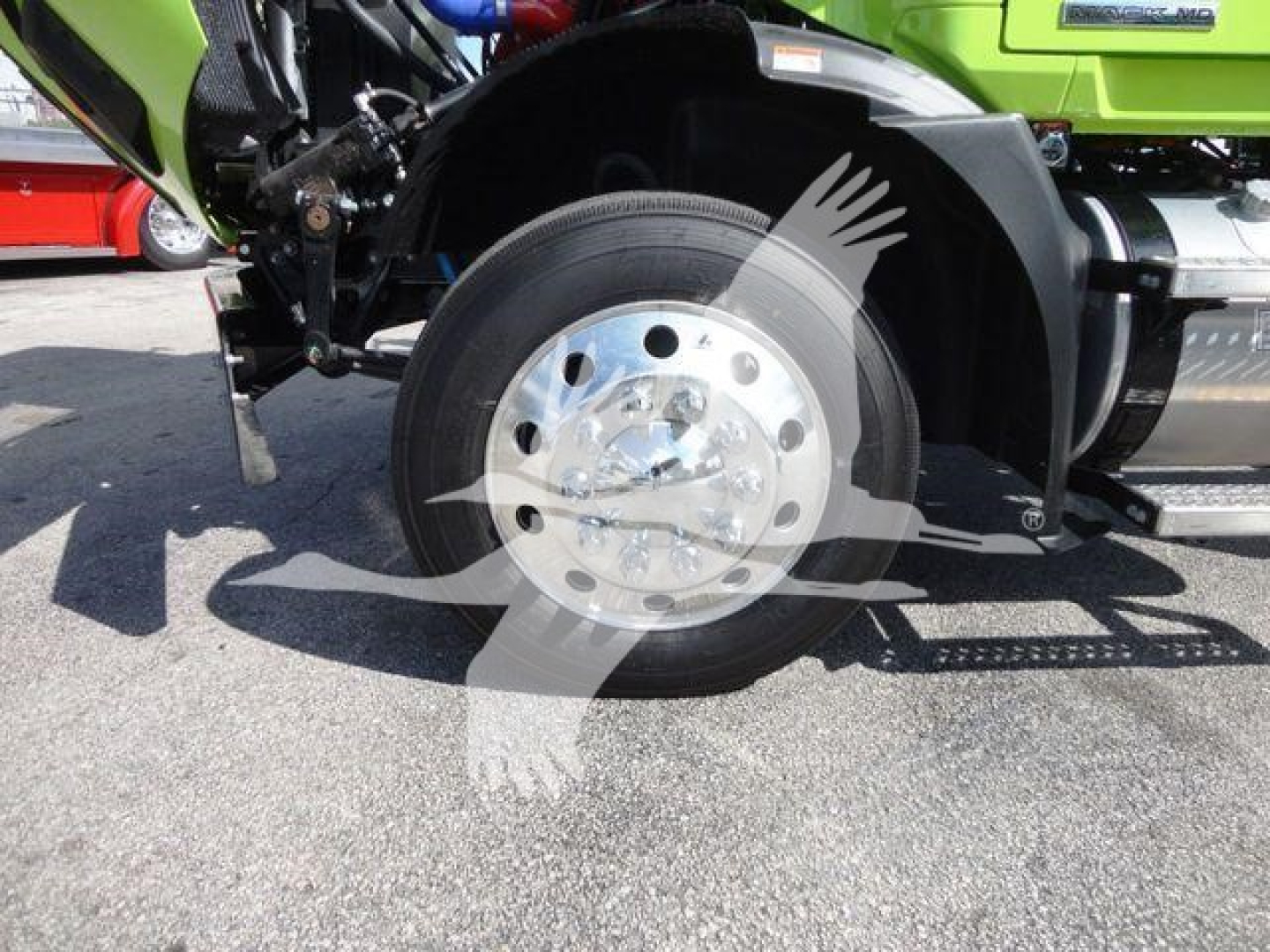 Mack MD6 truck front wheel and fender view showing polished hubcap, tire, and green body with rollback equipment
