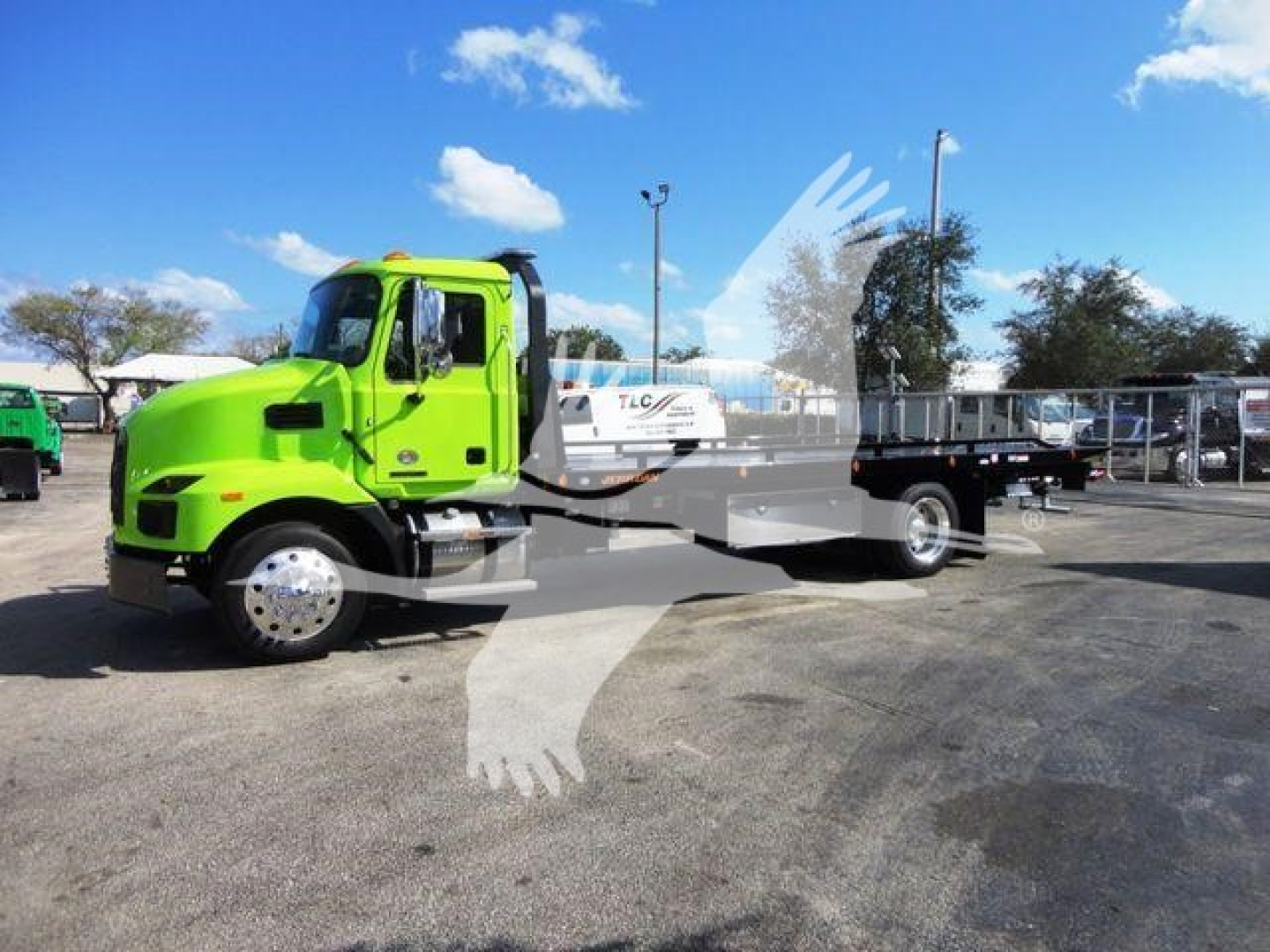 Green Mack MD6 rollback truck parked side view showing cab, flatbed, and equipment body.
