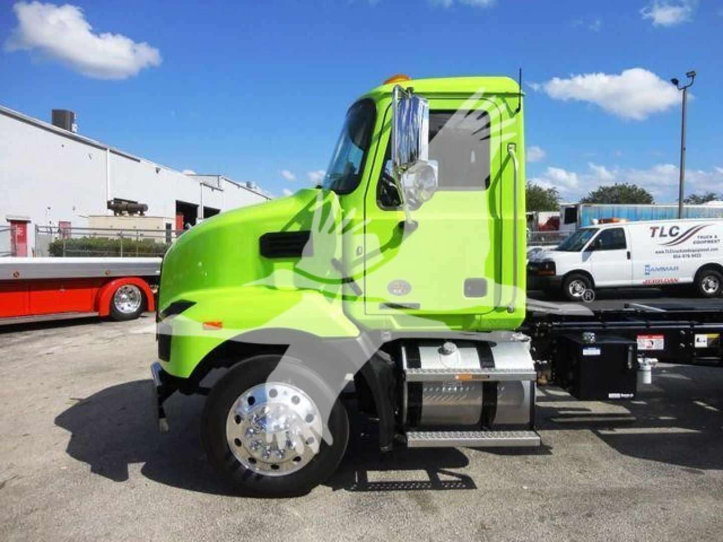 Bright green Mack MD6 rollback truck in side profile view with stock number J04366; text on the side of the truck not visible; background shows other trucks and a white building.