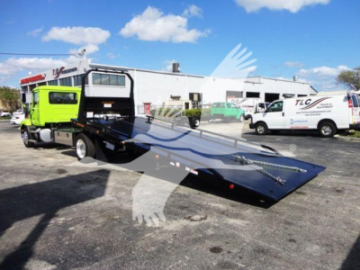 Flatbed tow truck with bright green cab and black ramp on a dealership lot.