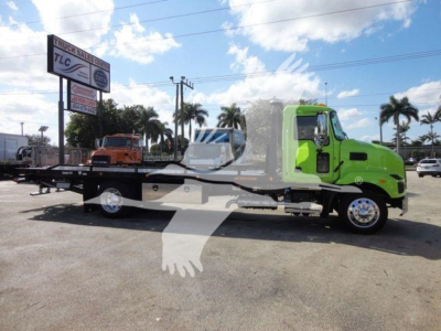 MD6 tow truck with a bright green cab and black flatbed, side view showing rollback equipment and a secondary orange truck on the bed, palm trees in background.