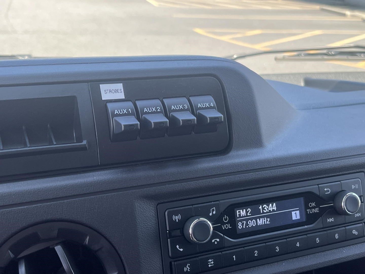 Ford E-350 dash showing auxiliary switches labeled AUX 1 to AUX 4 and radio display tuned to FM2 87.90 MHz.
